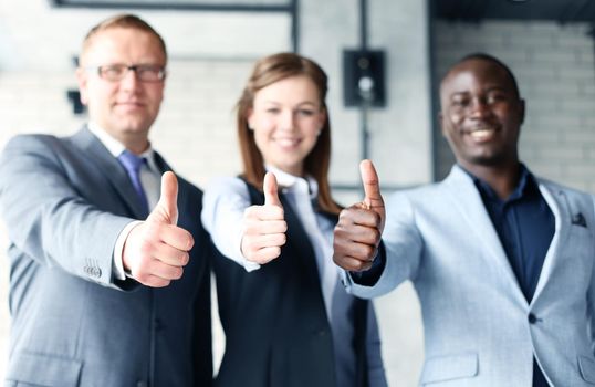Portrait of happy businesspeople standing in office showing thumb up