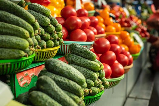 View over fresh organic cucumbers and tomatoes in sorted in baskets on the counter at the market. Raw veggies at the market.