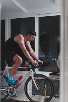 Man cycling on the machine trainer he is exercising in the home at night. Playing online bike racing game during coronavirus covid19 lockdown. New normal concept.