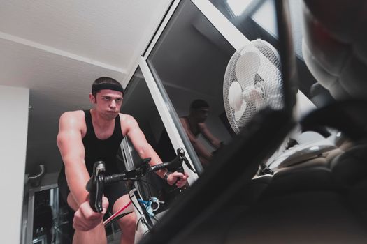 Man cycling on the machine trainer he is exercising in the home at night. Playing online bike racing game during coronavirus covid19 lockdown. New normal concept.