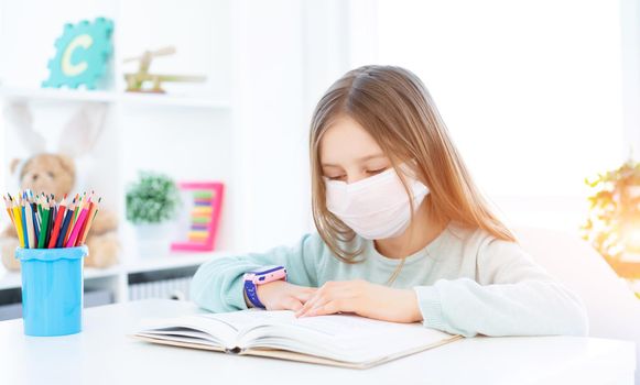 Cute schoolgirl in medical face mask studying at home