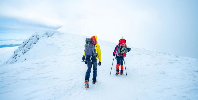 Couple of tourists trekking winter mountain top covered with snow