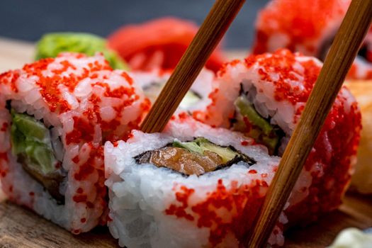 Closeup view on colorful set with sushi maki and wasabi. Person picks up traditional japanese roll with wooden chopstick. Oriental asian meal
