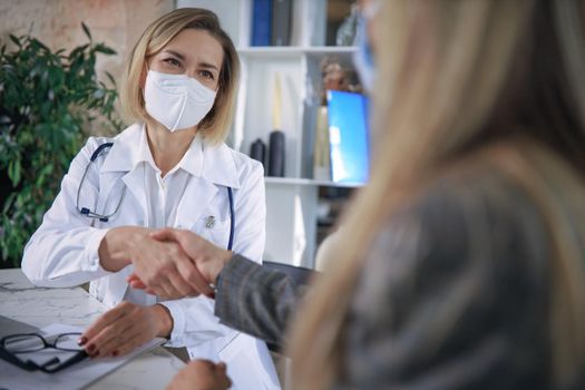 Cheerful female doctor psychologist shaking grateful patient hands after having a consultation meeting