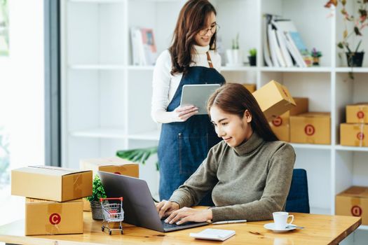 two happy women selling products online Start a small business owner using a laptop computer and tablet to calculate prices and prepare for postage