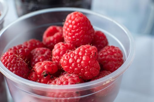 Picture of sweet, tasty, red and fresh raspberries are in the small plastic cup.