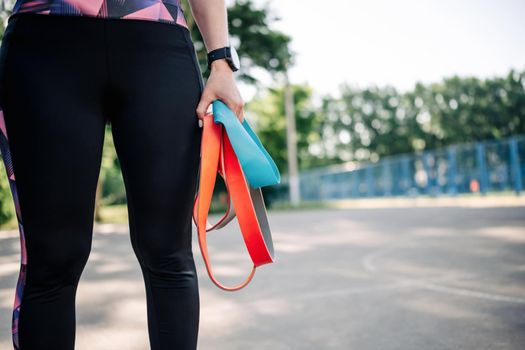 Young girl woman standing at stadium and holding in her hands set of colorful rubber elastic bands going to exercising. Active training for female with additional sport equipment outside
