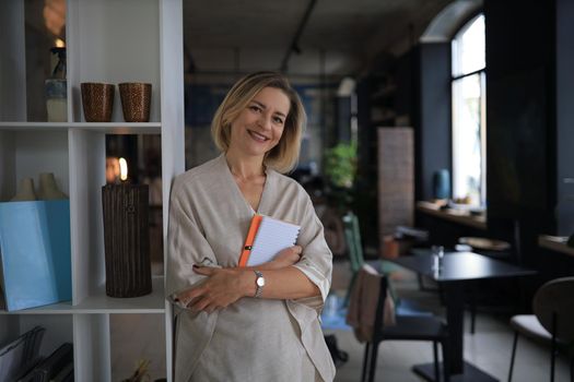 Confident stylish european middle aged woman standing at workplace, executive leader manager looking at camera