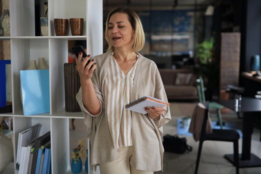 Beautiful business woman is using her smartphone with smile while standing in the office