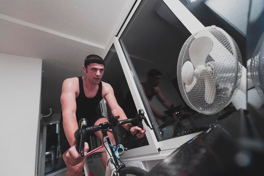 Man cycling on the machine trainer he is exercising in the home at night. Playing online bike racing game during coronavirus covid19 lockdown. New normal concept.