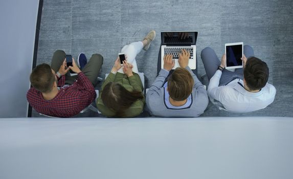 Group of attractive young people sitting on the floor using a laptop, Tablet PC, smart phones, smiling.