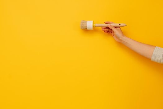 Woman hand holding wooden paint brush on yellow background with copy space. Concept of creativity, improvement and inspiration. Working tool for home design project