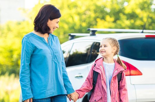 Mother with daughter going back to school holding hands outdoors with car
