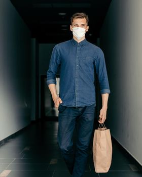 young man in a protective mask walking along a city street. coronavirus in the city