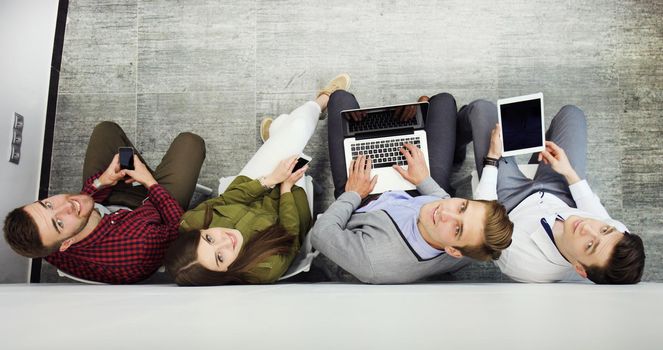 Group of attractive young people sitting on the floor using a laptop, Tablet PC, smart phones, smiling.