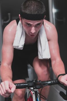 Man cycling on the machine trainer he is exercising in the home at night. Playing online bike racing game during coronavirus covid19 lockdown. New normal concept.