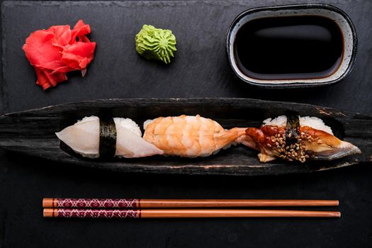 Elegant served sushi set composition with fresh shrimp and raw salmon on black plate with ginger, wasabi and soy sauce shooting from above. Traditional japanese meal with wooden chopstick