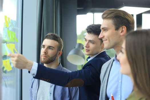 young creative startup business people on meeting at modern office making plans and projects with post stickers on glass
