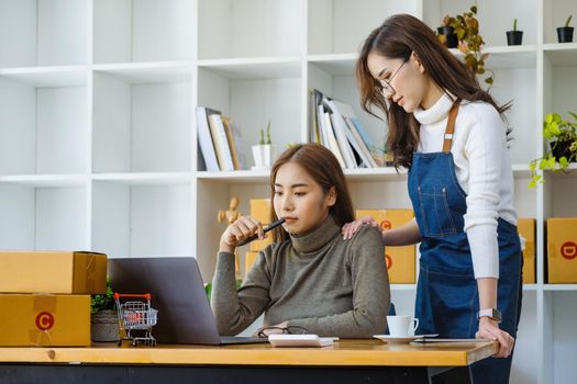 two happy women selling products online Start a small business owner using a laptop computer and calculate prices and prepare for postage