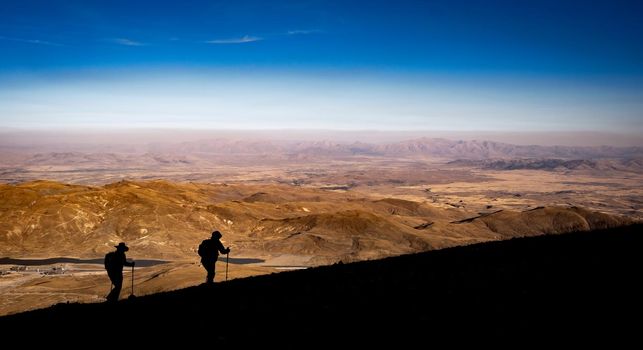 Silhouettes of two people during hiking on volcano Erciyes in Turkey in sunrise time. People climbing to mountain and looking from the top on beautiful hills. Scenery Kayseri landscapes with blue sky