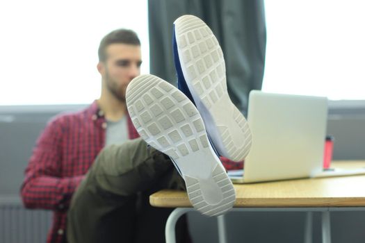 Portrait of a very relaxed young designer leaning back on his desk and putting his feet up his desk at the office.