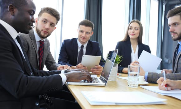 Young handsome woman gesturing and discussing something while his coworkers listening to him sitting at the office table
