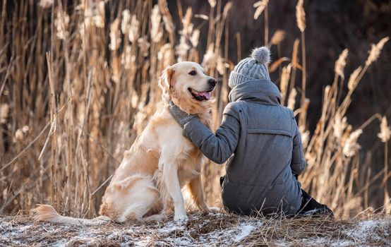 Woman owner sitting on the ground with golden retriever dog and petting him during early spring walk outdoors . Portrait of girl with doggy pet labrador together at the nature