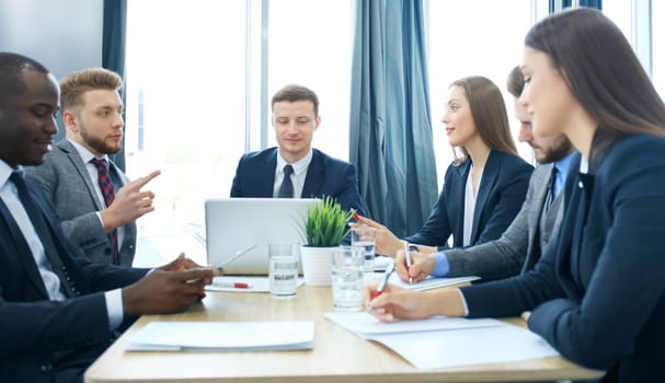 Young handsome man gesturing and discussing something while his coworkers listening to him sitting at the office table