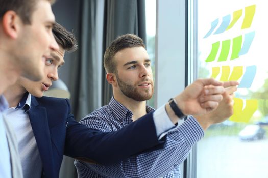 young creative startup business people on meeting at modern office making plans and projects with post stickers on glass