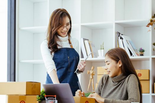 selling products online, the focus is on the face of a woman in white pointing to a friend to write down the shipping address for the customer and prepare it for postage