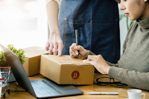 Two happy women selling products online. Start a small business owner with a pen to write down the addresses of customers and prepare them for postage