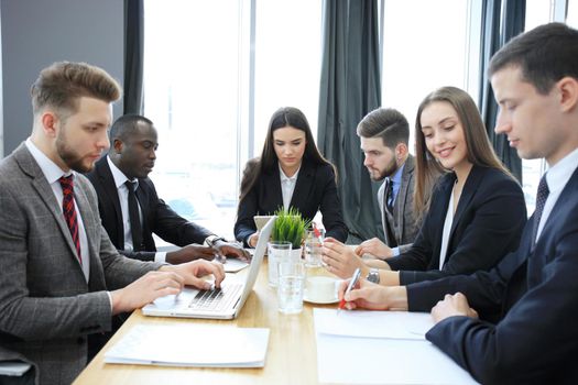 Young handsome woman gesturing and discussing something while his coworkers listening to him sitting at the office table