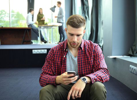 Smiling young man using smart phone in the office.
