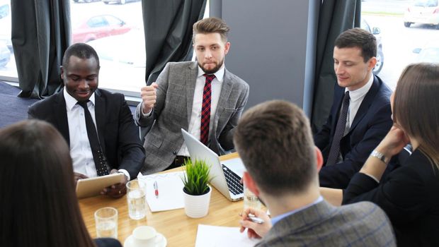 Brainstorm. Group of business people looking at the laptop together. One business woman looking at camera.