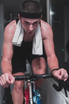 Man cycling on the machine trainer he is exercising in the home at night. Playing online bike racing game during coronavirus covid19 lockdown. New normal concept.