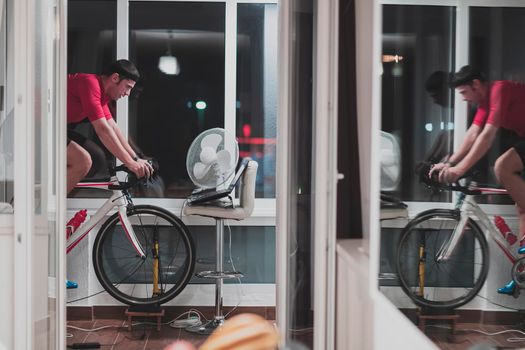 Man cycling on the machine trainer he is exercising in the home at night. Playing online bike racing game during coronavirus covid19 lockdown. New normal concept.