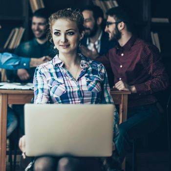 young successful financial administrator woman with laptop on background of business partners handshaking