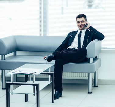 businessman sits in the lobby of a modern office and talking on the phone.the photo has a empty space for your text