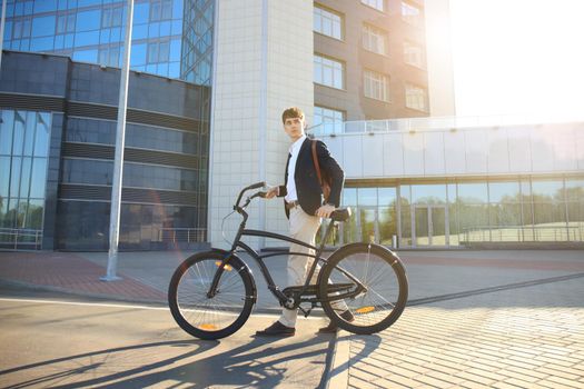 Confident young businessman walking with bicycle on the street in town.
