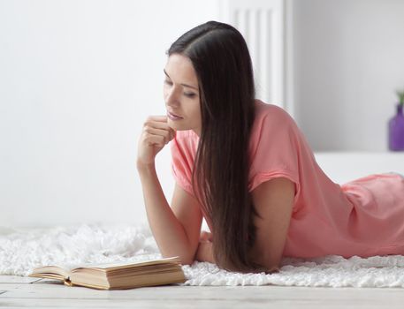 portrait of young girl reading book lying on floor in living room.