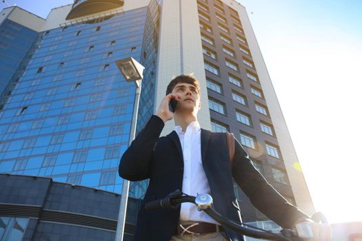 Young businessman with bicycle and smartphone on city street.