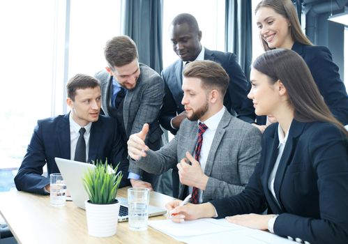 Brainstorm. Group of business people looking at the laptop together. One business woman looking at camera