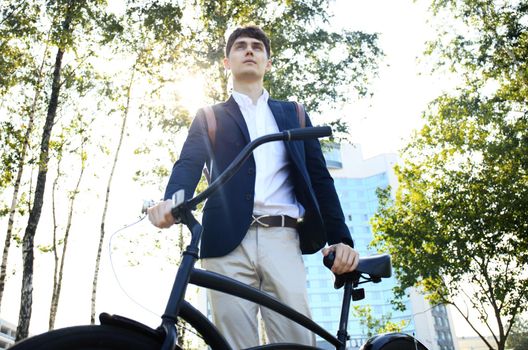 Confident young businessman walking with bicycle on the street in town.