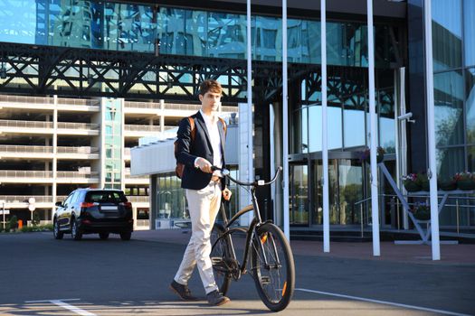 Confident young businessman walking with bicycle on the street in town.