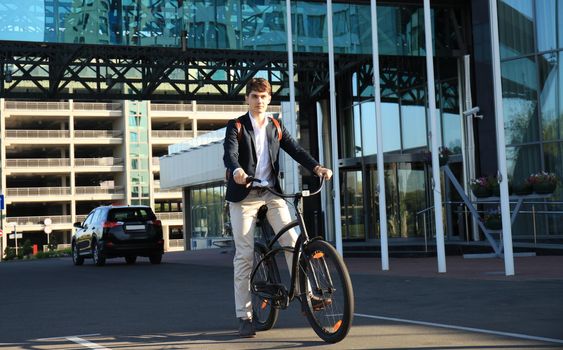 Confident young businessman walking with bicycle on the street in town.