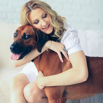 Happy pregnant woman and a dog sitting on a couch cuddling cute