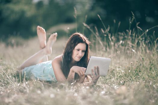 cute girl with digital tablet lying on lawn on summer day. people and technology