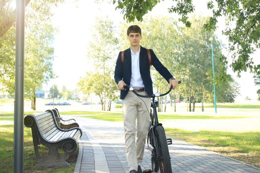 Confident young businessman walking with bicycle on the street in town.