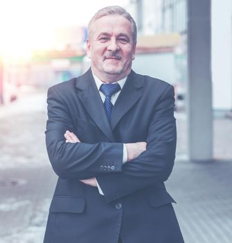 portrait of a successful businessman standing with crossed hands in front of him, on the background of office building