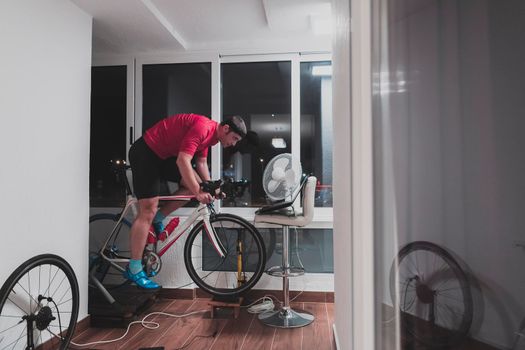 Man cycling on the machine trainer he is exercising in the home at night. Playing online bike racing game during coronavirus covid19 lockdown. New normal concept.